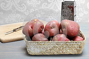 Natural red potatoes in a basket with utensils to prepare in background