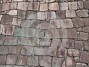 Natural rock blockwork in a wall with green and lilac colours caused by algae and lichen growth