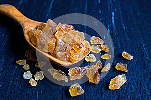 Natural rock sugar in wooden spoon on rustic table