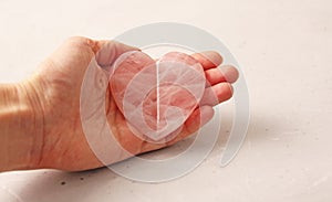 Natural rose quartz heart stone is on a woman`s hand, in the palm of her hand, on a light background. Natural stones, crystals fo