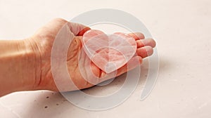Natural rose quartz heart stone is on a woman`s hand, in the palm of her hand, on a light background. Natural stones, crystals fo