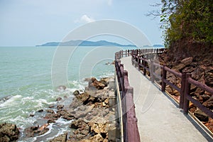 Natural scenic shot of rocky cliff with greenery tree on the sea and ocean wave which the walking path bridge shows beauty tourism