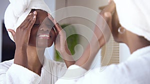 Natural skin care morning routine. Young black woman applying moisturizing cream with with gentle movements,