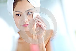 Natural skincare. An attactive young Asian woman applying moisturizer with a towel on her head.