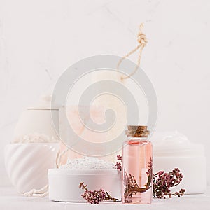 Natural spa cosmetics with pink rose oil, salt, soap and lavender flowers closeup on white wood background, interior, border.