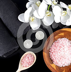 Natural spa ingredients with white orchid flowers ,black towel and pink salt on a wooden bowl on a black background
