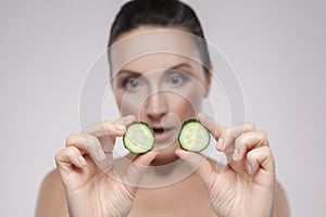 Natural spa treatment. Portrait of beautiful mature woman holding pieces of cucumber, looking for them and not believe while
