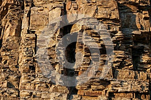 Close-up rufous stony wall with layered uneven hollowed-out surface.