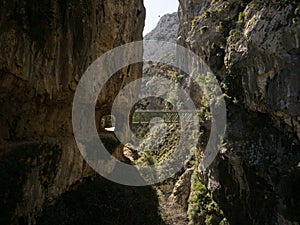 Natural tunnel and green steel bridge on hiking trail path Senda del Cares canyon in Picos de Europa mountains Spain photo