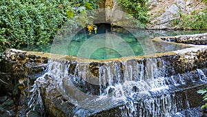 Natural waters and water pool coming from the rocky cave in the mountain