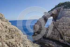 Natural window in stone in Korakonissi and people jumping in the water from a cliff