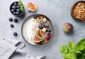 Natural yogurt with granola, berries and figs in a black bowl on a blue background with mint. Healthy and nutritious breakfast