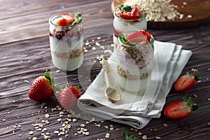 Natural yogurt in little jar with jam, muesli and fresh strawberry, mint leaves. Healthy breakfast concept.