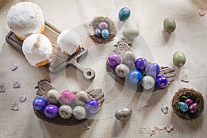 Naturally dyed Easter quail and hen`s eggs, nest, Easter cakes, wooden hearts on linen background, flat lay