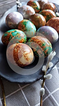 Naturally painted Easter eggs in a black clay plate on a rustic wooden background