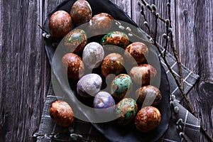 Naturally painted Easter eggs in a black clay plate on a rustic wooden background