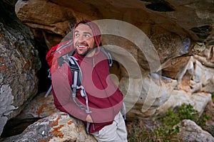 Nature, cave and man with smile, backpack and happiness in mountain or rock for adventure and freedom. Hiking, earth and