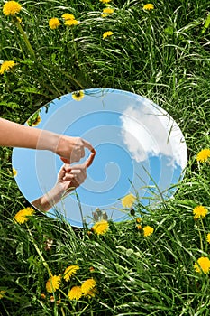 hand touching sky reflection in mirror on field