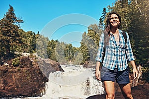 Nature guarantees happiness. an attractive young woman standing next to a rocky river and waterfall.