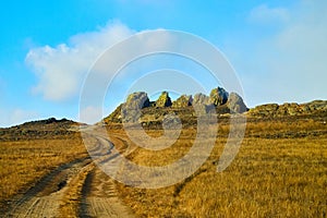 Nature landscape with golden glass, old rural road, hills and blue sky with white clouds on background in a nice day or