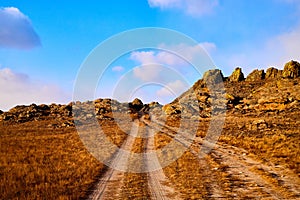 Nature landscape with golden glass, old rural road, hills and blue sky with white clouds on background in a nice day or