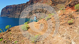 Nature landscape. Woman walks on dangerous road along volcanic rock formations. Blue sky. Amazing ocean beach. Scenic