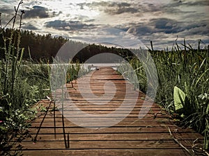 Nature landscape with wooden pantoon, green grass, lake and cloudy sky before rain