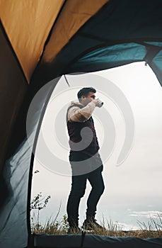Nature is a lot cheaper than therapy. a young man drinking coffee while camping in the wilderness.