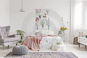 Nature lover`s bright bedroom interior with a wall art of flowers and birds painted on a fabric above a bed which is dressed in g