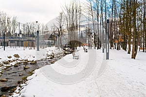 Nature park in the city covered with snow through which a mountain stream flows, on the shore there are stones. Visible people wal