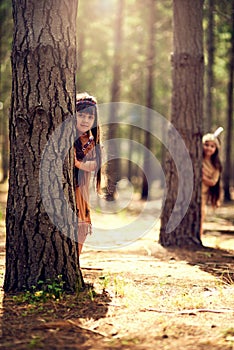 Nature is a part of our heritage. Portrait of two little girls hiding behind trees while playing dressup in the woods.