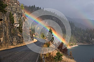 Nature scene after rain with a highway surrounded by cliffs and mountains by the sea with a rainbow