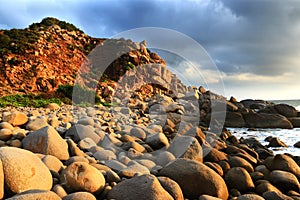 Nature Seascape with Eggshaped Rocks on A Wild Beach and A Rocky Cliff at Dramatic Sunrise photo