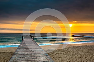 Nature Seascape with A Pier on Sandy Beach and The Sun at Sunrise