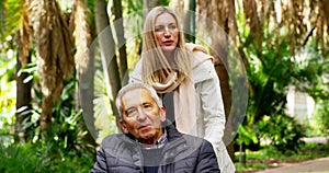 Nature, senior man in wheelchair with woman on garden path, quality time with daughter on outdoor walk. Retirement