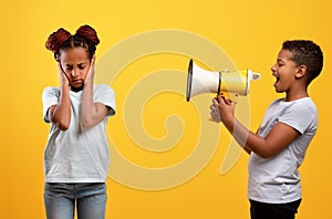 Naughty afro-american boy yelling at his sister, using megaphone