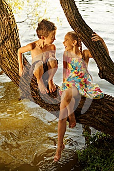 naughty boy and girl sitting on a branch over water, laughing out loud, having fun talking