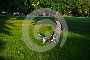 The naughty boy plays with doggy on a green glade in park.