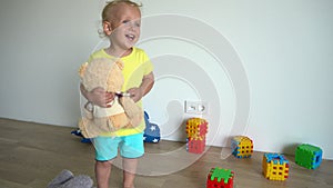 Naughty child boy holding teddy bear destroy tower built from colorful blocks