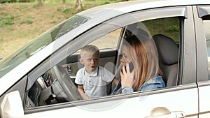 Naughty child interferes with mom in a car, he closes her eyes with his hands.