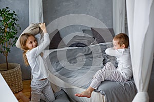 Naughty children a little boy and a girl in pajamas had a pillow fight on the bed in a gray bedroom. They like this game. Home is