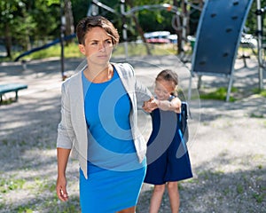 The naughty girl pulls her mother by the hand, wanting to stay on the playground. The capricious daughter resists and