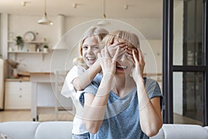 Naughty little girl closing eyes of laughing mother with palms