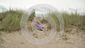 Naughty little girl falling down from sandy dune. 5 years old child having fun