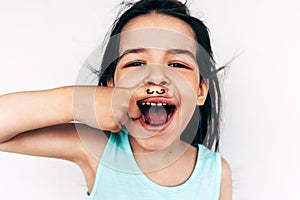 Naughty little girl grimacing and smiling broadly with mustache drawing on her index finger put it under the nose. Adorable child