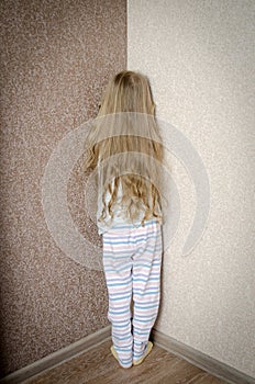 Naughty little girl is standing in the corner punished