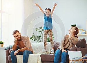 Naughty, mischievous, child girl jumping, laughing and having fun, parents stressed with  headache photo