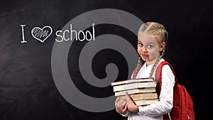 Naughty schoolgirl with books standing near blackboard, I love school phrase