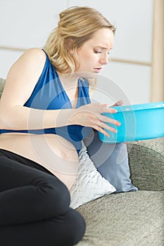 nauseous pregnant woman on sofa holding plastic bowl