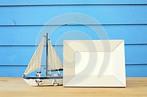 Nautical concept with empty photo frame and sail boat over wooden table. For photography montage.